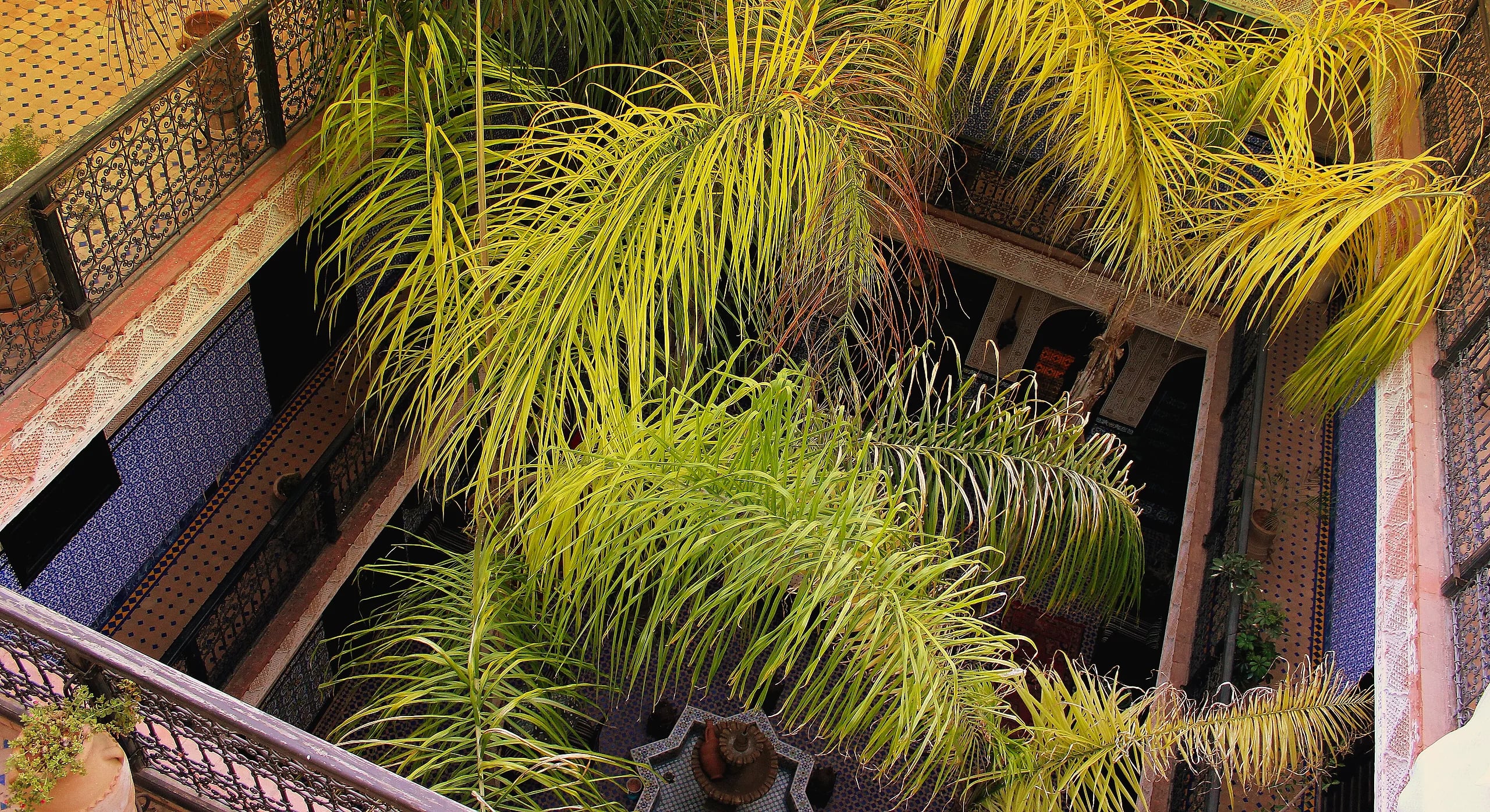 Looking down into a riad courtyard in Marrakech: palms, tiled galleries and a star-shaped fountain